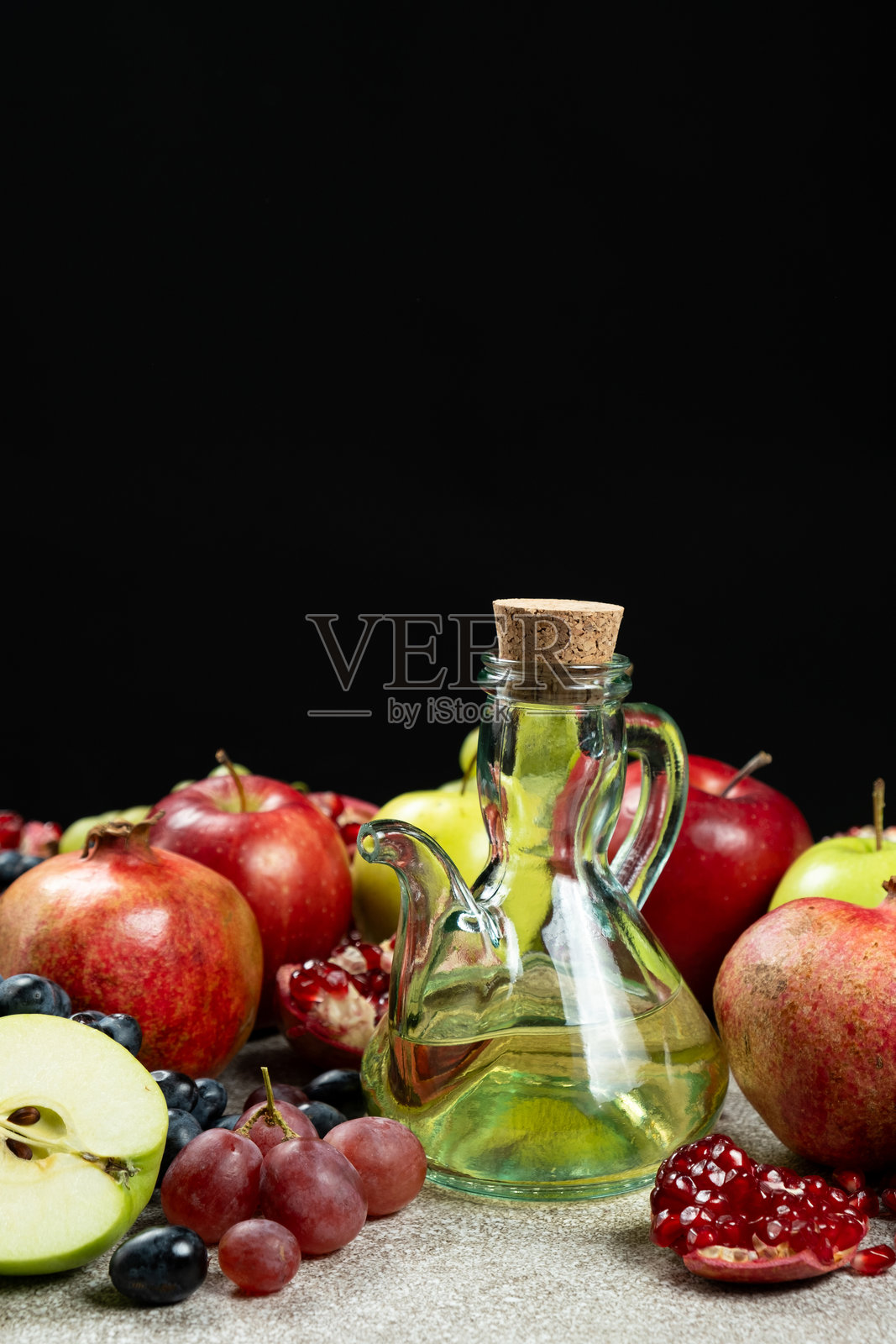 黑色背景下,水果旁的玻璃醋瓶中的醋照片摄影图片