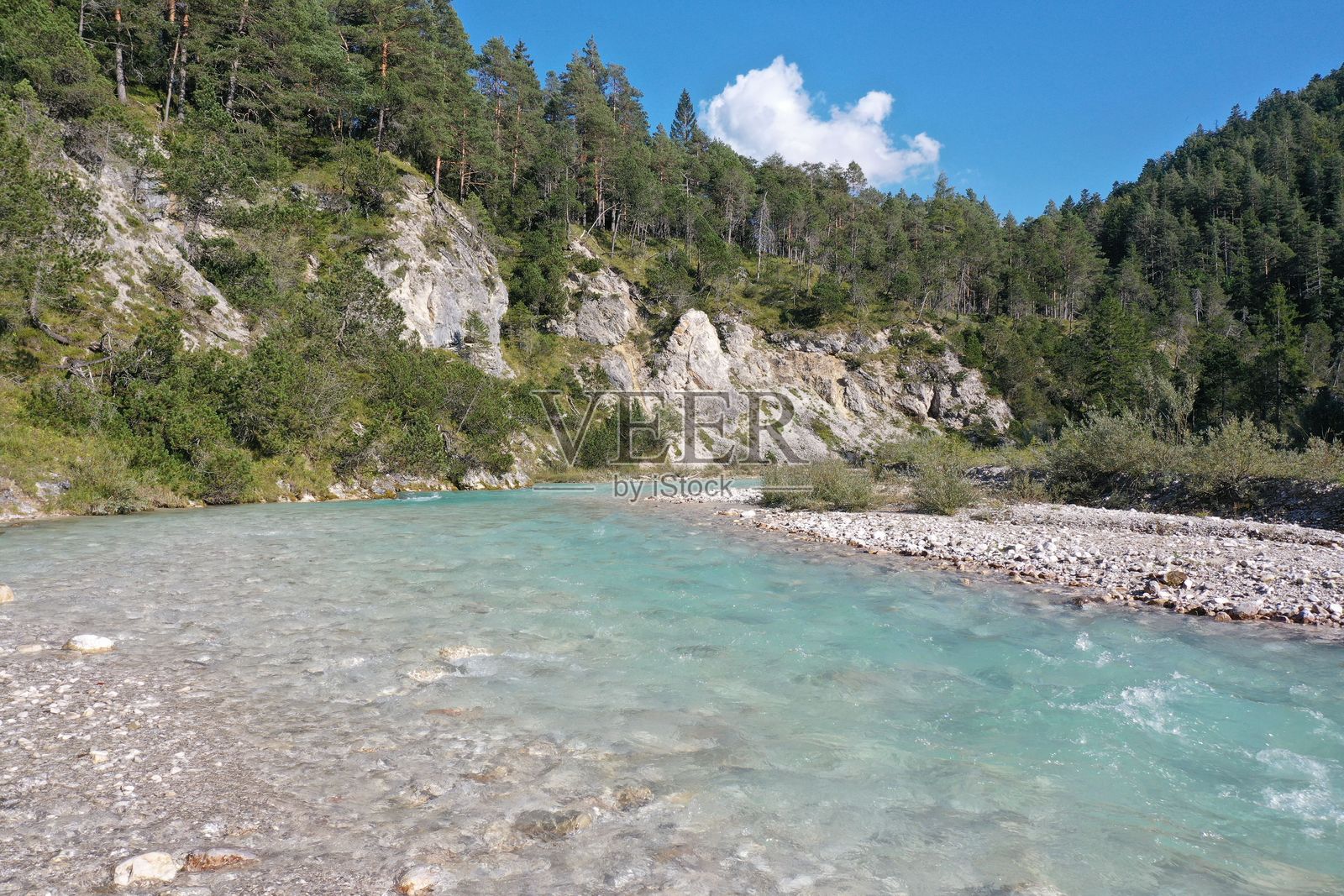 一条碧绿色的河流穿过郁郁葱葱的森林景观,映衬着晴朗的蓝天。照片摄影图片