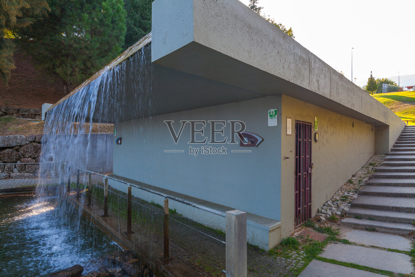 现代混凝土建筑,设有瀑布景观和旁边的楼梯,位于公园环境中照片摄影图片