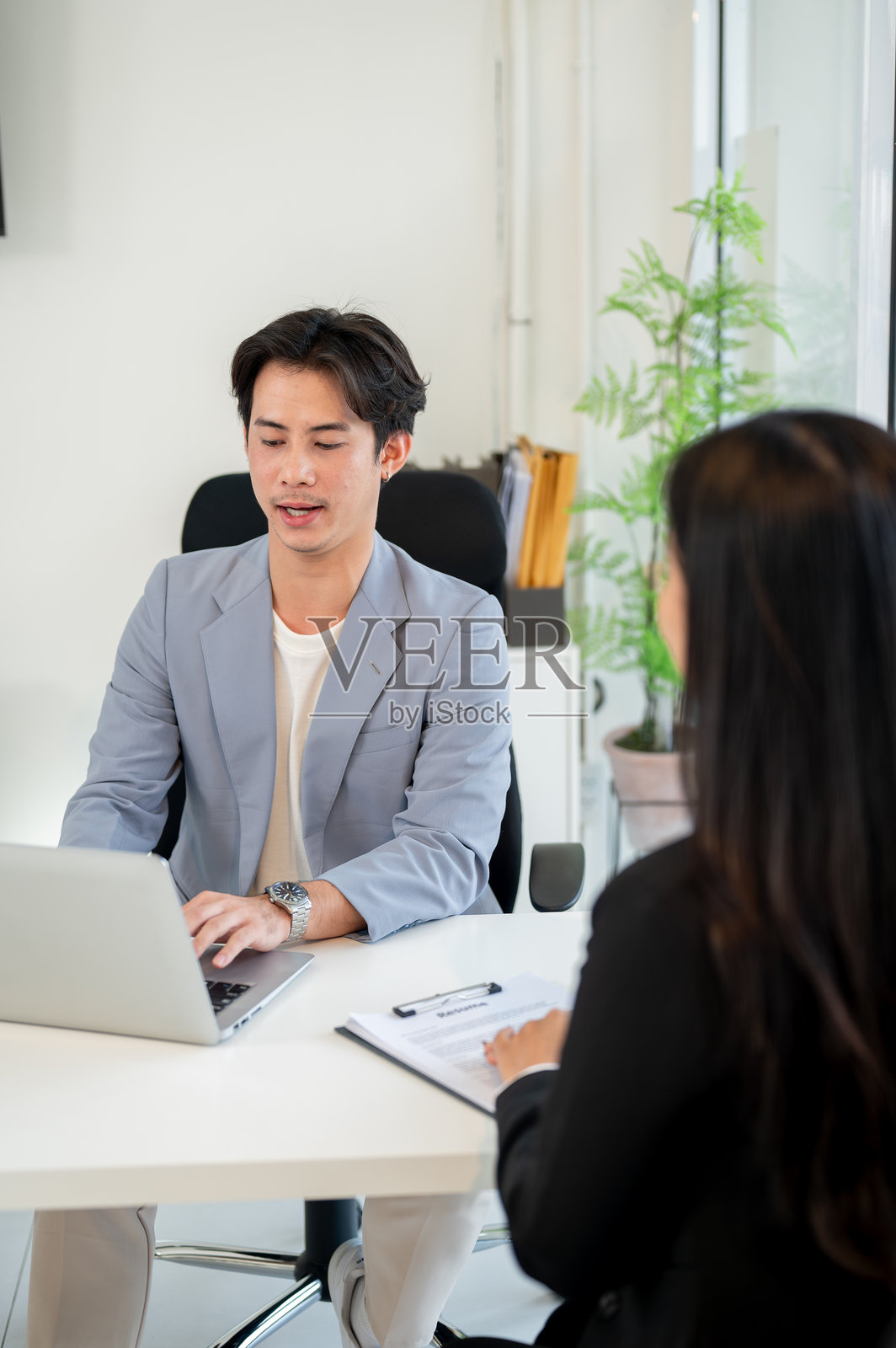 一位专业的亚洲商人在办公室里使用笔记本电脑面试候选人。照片摄影图片