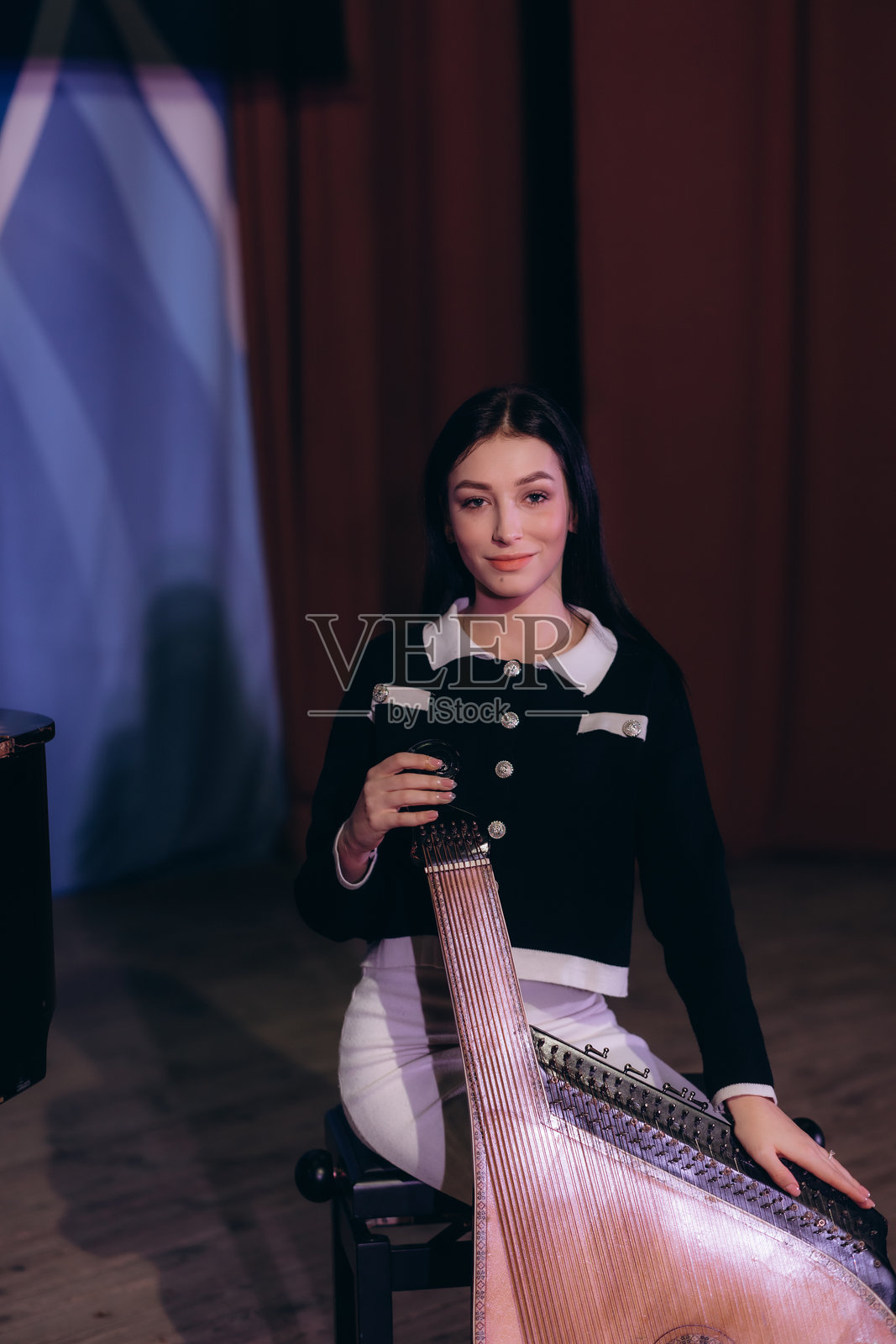 美丽的精灵女孩在阳光照耀的绿色森林背景中站立。身穿古老复古服装的女人正在弹奏竖琴。照片摄影图片