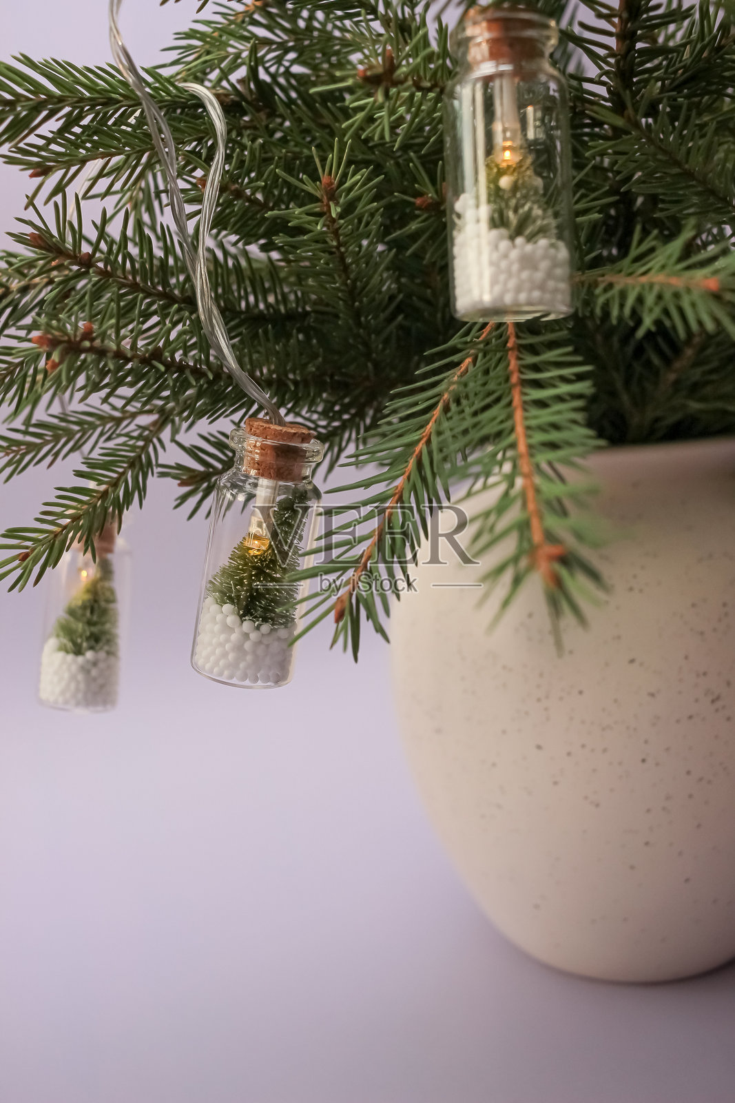 用冷杉树枝装饰的花瓶,上面装饰着与众不同的创意圣诞灯,在冷杉树和雪中形成一个玻璃瓶。喜庆的新年装饰照片摄影图片