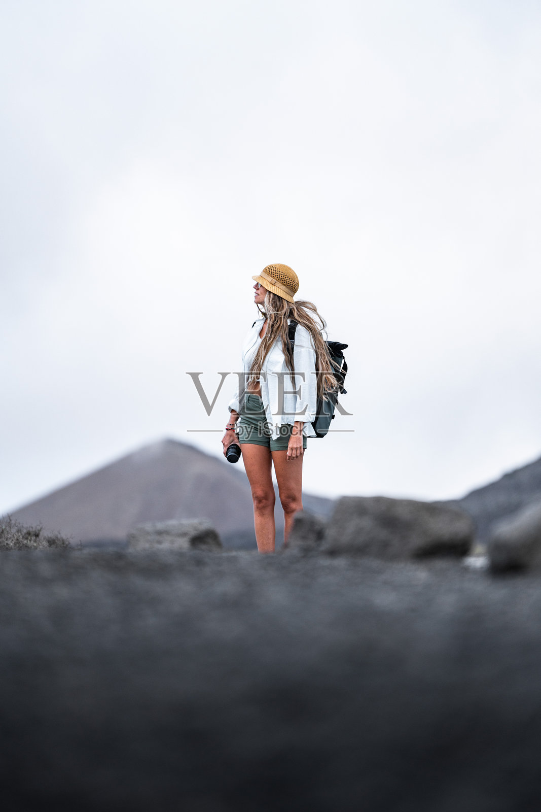 女性在多云天气中手持相机探索火山景观照片摄影图片