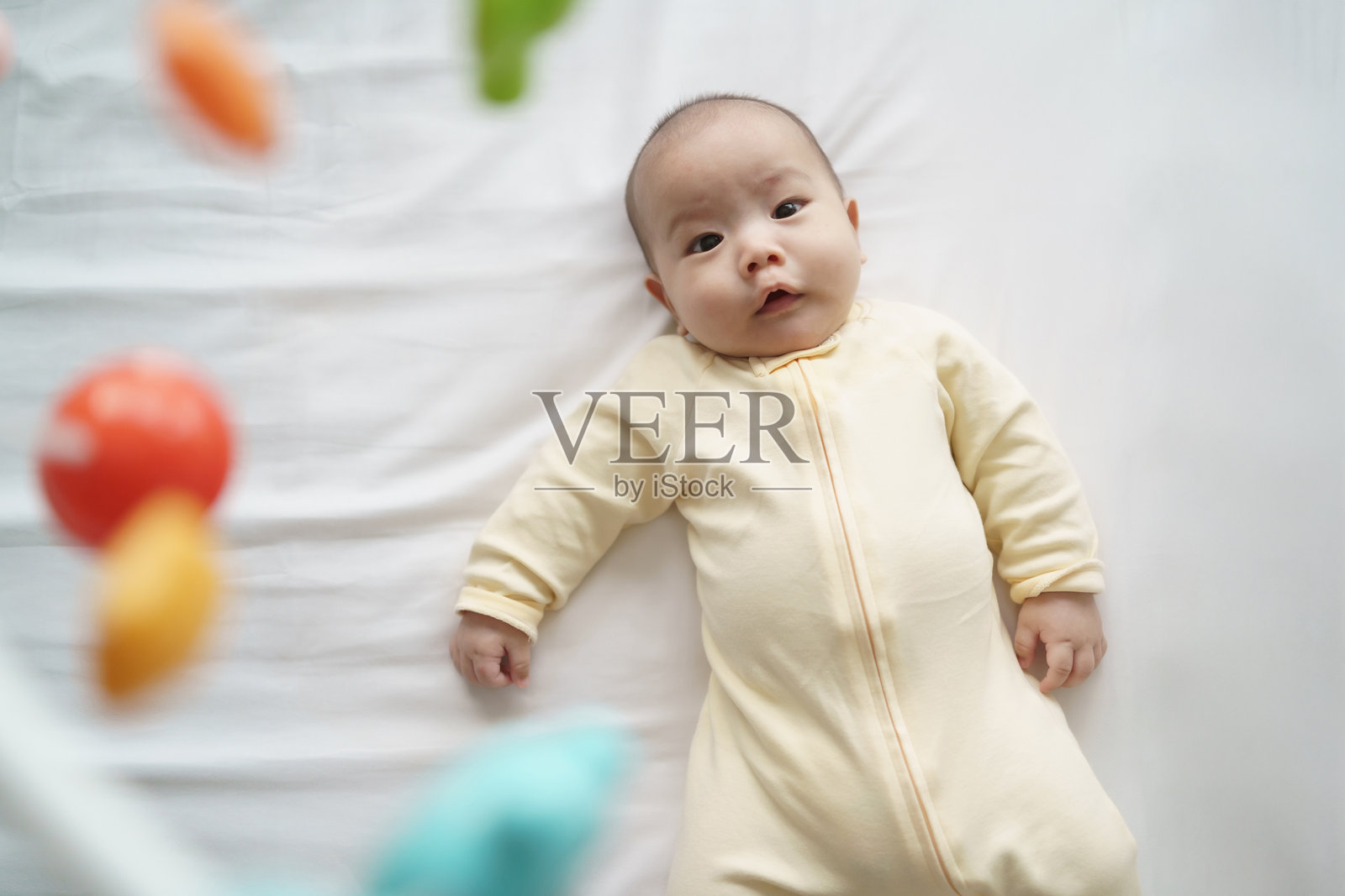 亚洲宝宝躺在婴儿床上,好奇而惊奇地仰望着悬挂的玩具。照片摄影图片