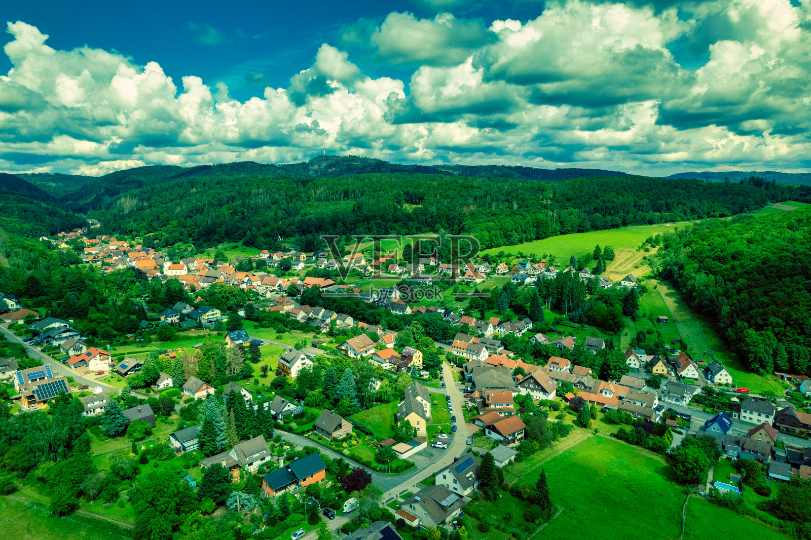 生机勃勃的德国村庄坐落在一个被郁郁葱葱的绿树和如画的山脉环绕的山谷中,阳光明媚。照片摄影图片