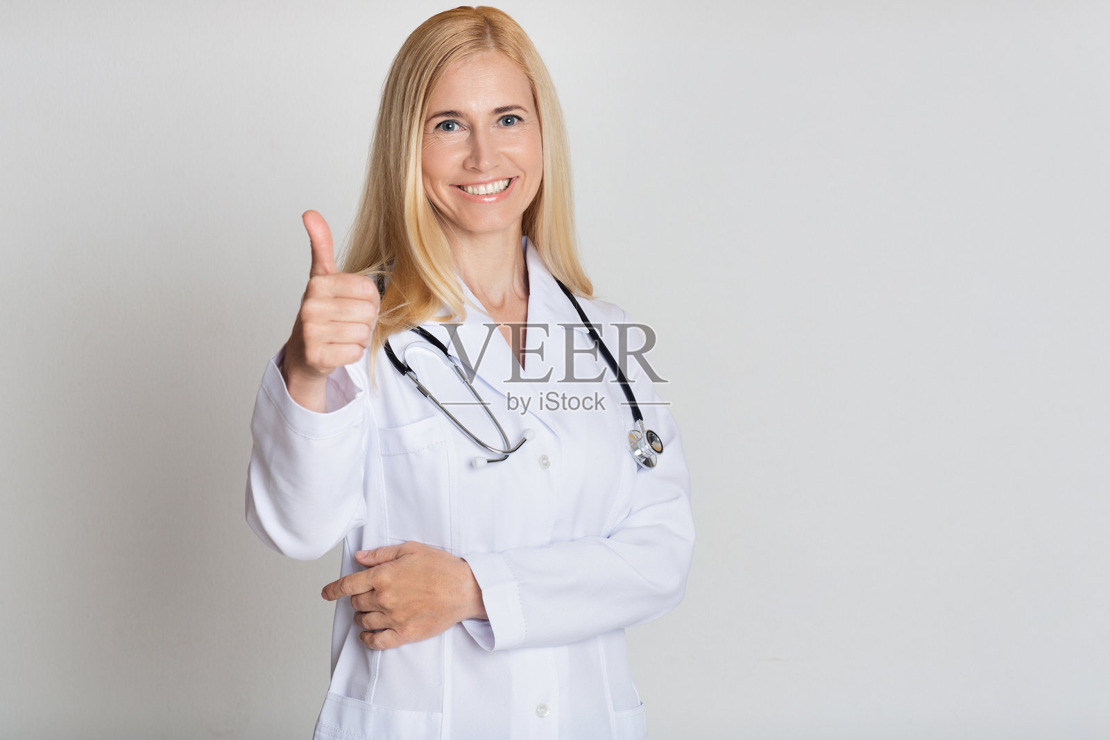 医生拿着听诊器在灰色背景下竖起大拇指照片摄影图片