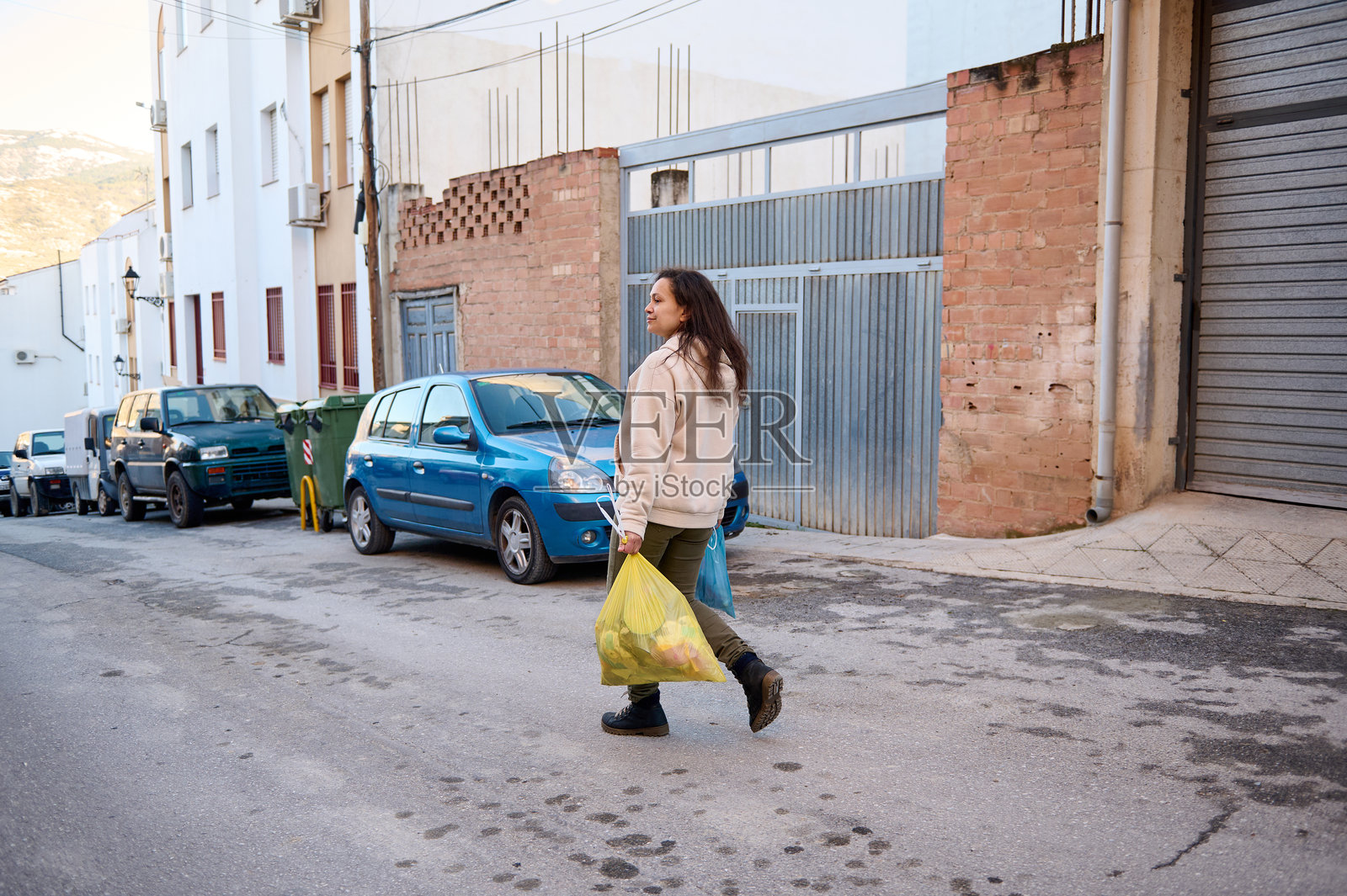 女人在城市街道上提着垃圾袋,周围停着汽车照片摄影图片