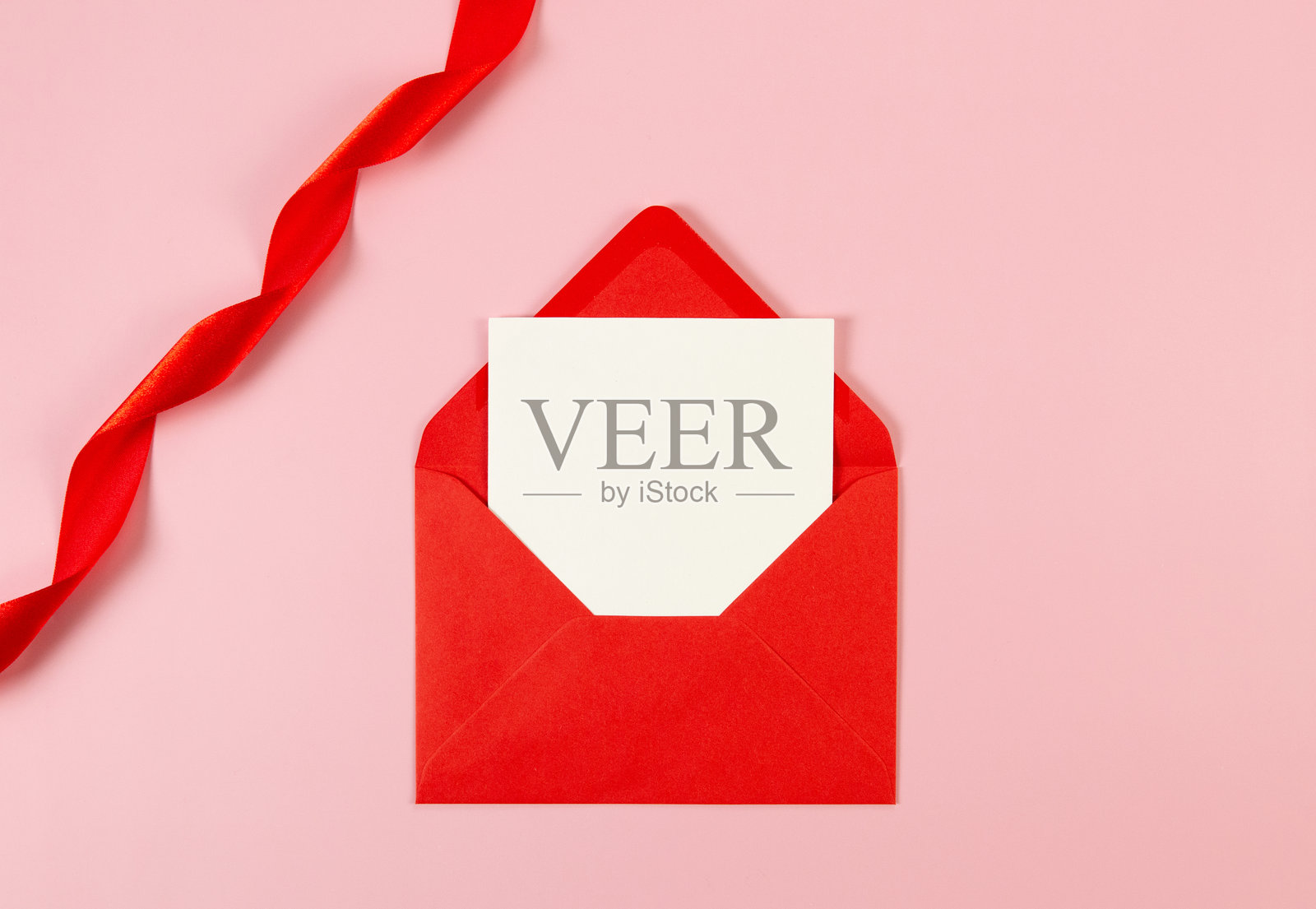 粉色背景上俯视红色信封、白色卡片和红色丝带。情人节,爱。闪亮的卷状面料,丝绸和缎子材质。照片摄影图片