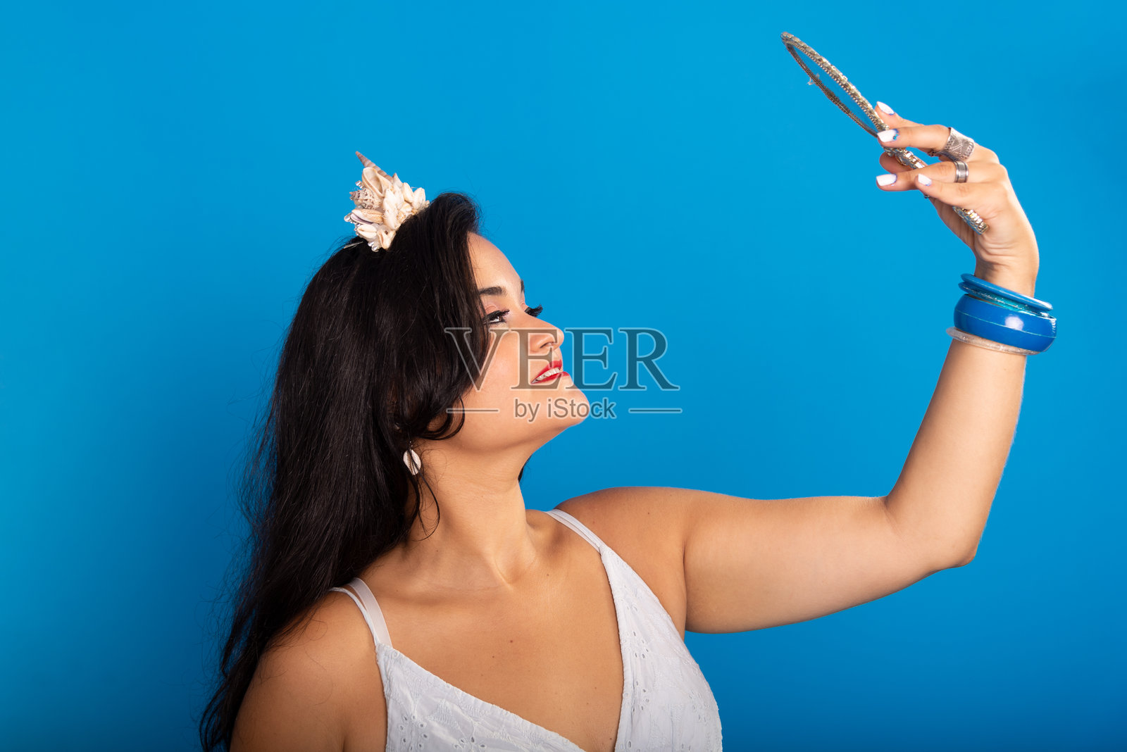 美丽的黑头发女人的肖像,穿着白色的衣服,拿着镜子,看着镜子。照片摄影图片