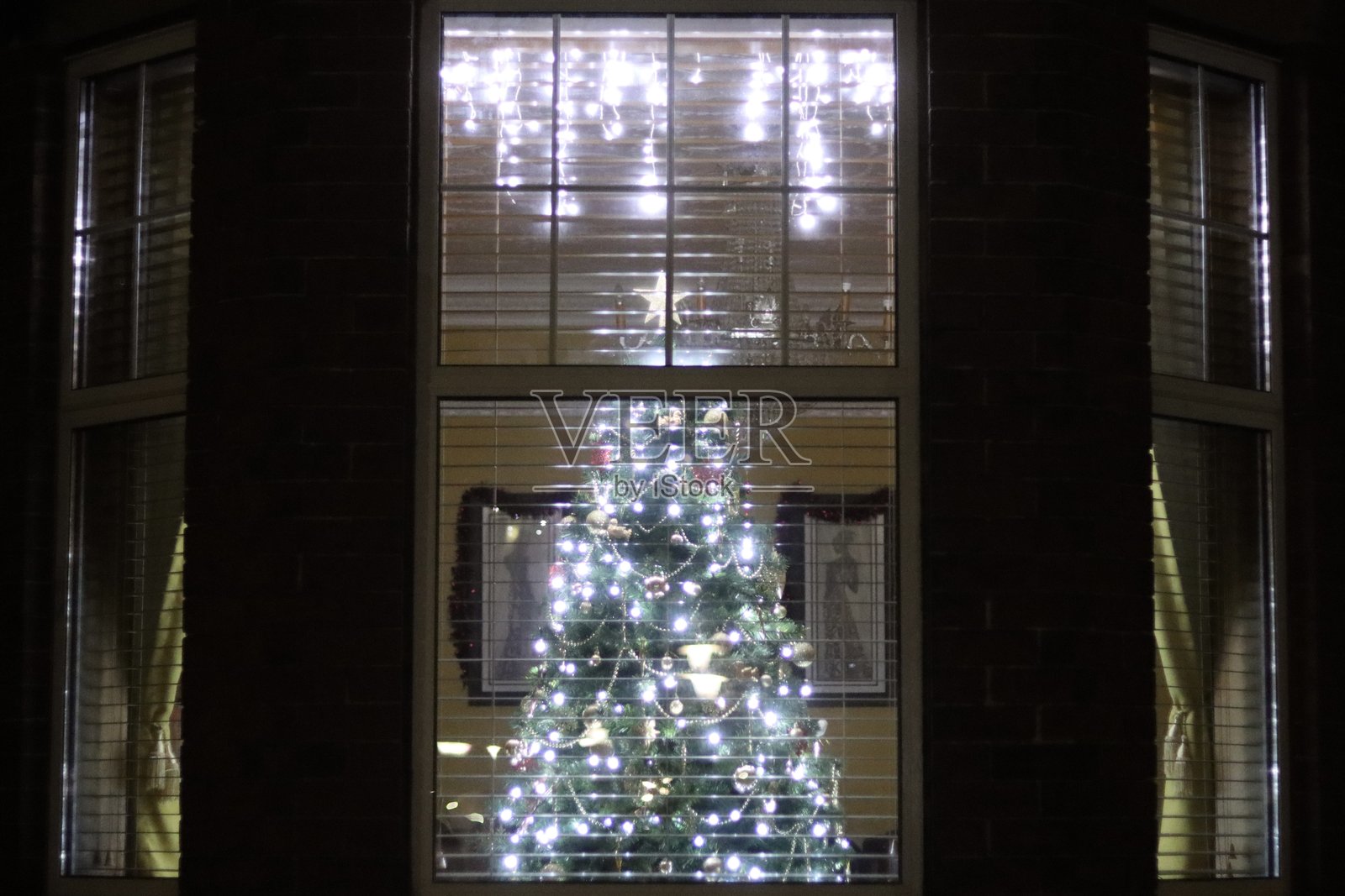 圣诞树在晚上透过房子的窗户,挂满了灯和装饰品照片摄影图片
