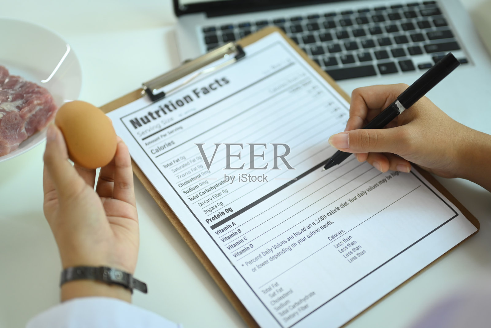 特写:营养师拿着鸡蛋,写着饮食计划,在工作场所创造健康的食物选择。照片摄影图片