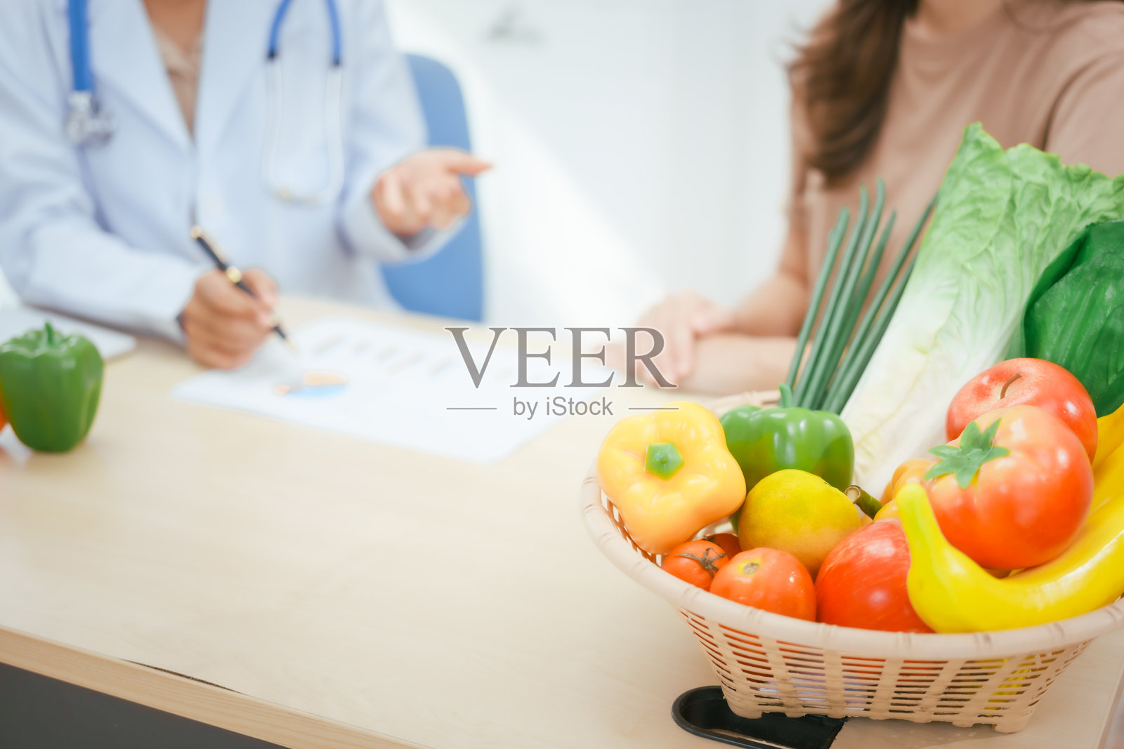 一位年轻女性营养专家在医院的办公桌前工作,咨询女性患者关于吃蔬菜和水果,推广健康饮食,提供有效减重和健康的指导。照片摄影图片