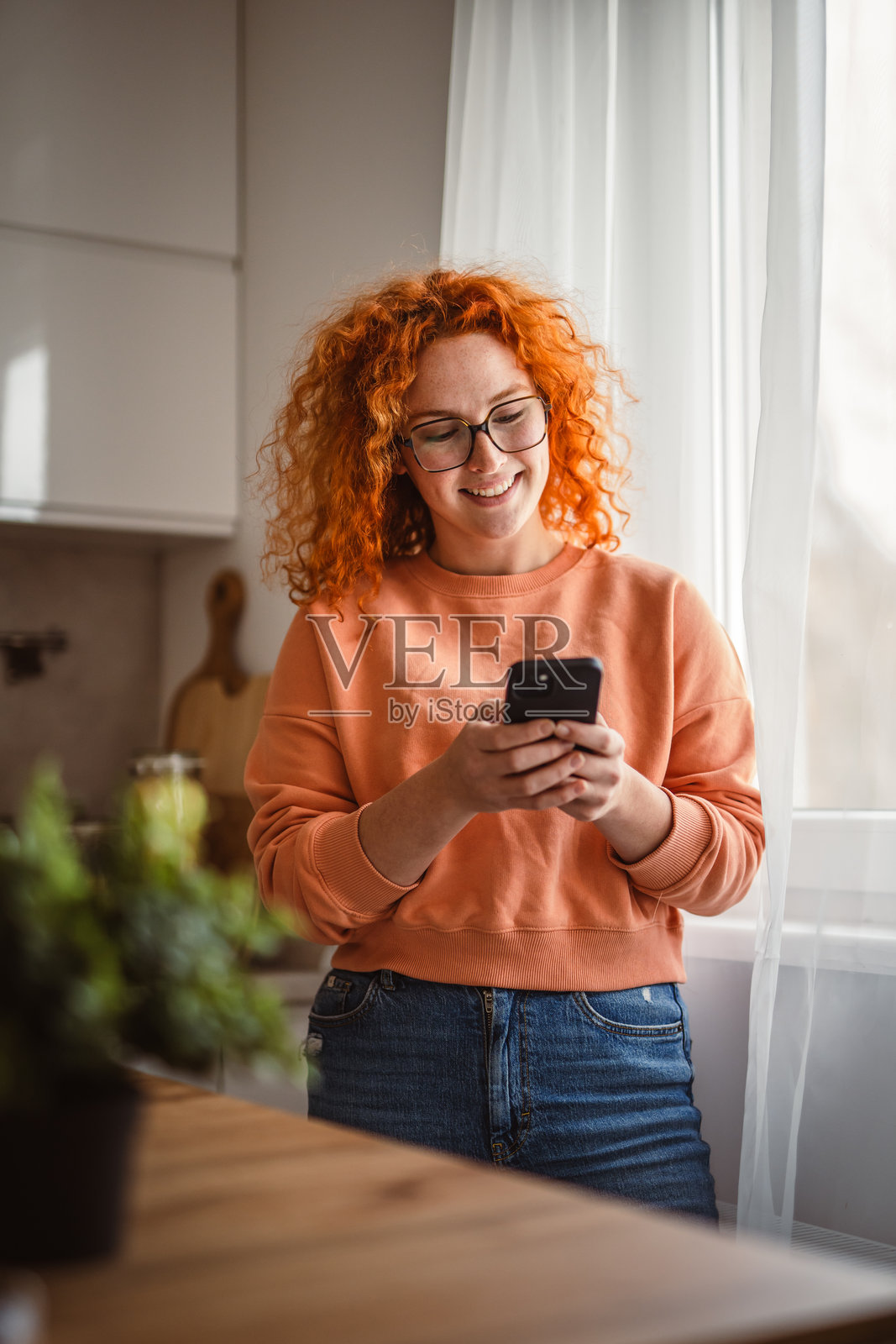 美丽女性在厨房里站着使用手机的肖像照片摄影图片
