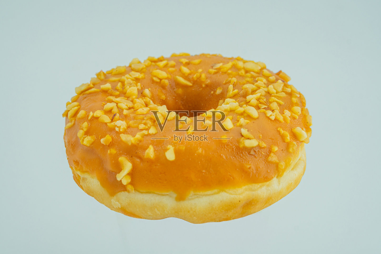 一只光滑的甜甜圈,上面撒有黄色糖屑,背景为浅色。照片摄影图片
