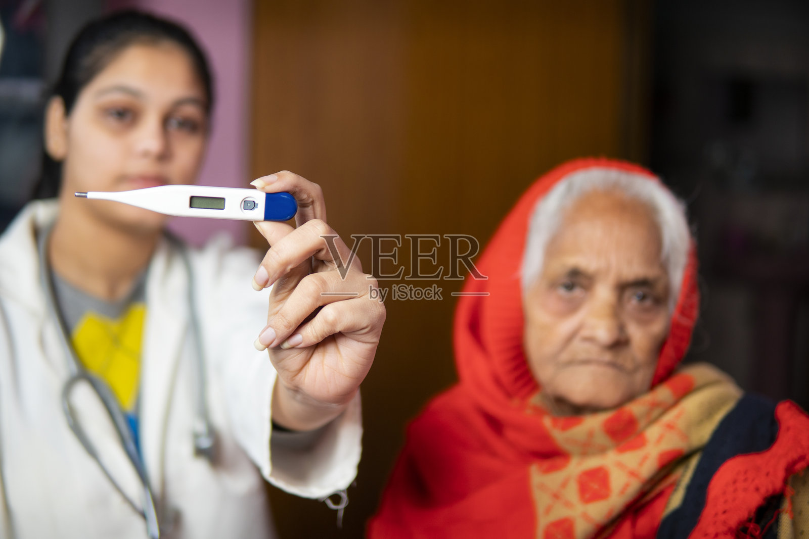 女医生在家中用温度计为生病的老年女性测量体温。照片摄影图片