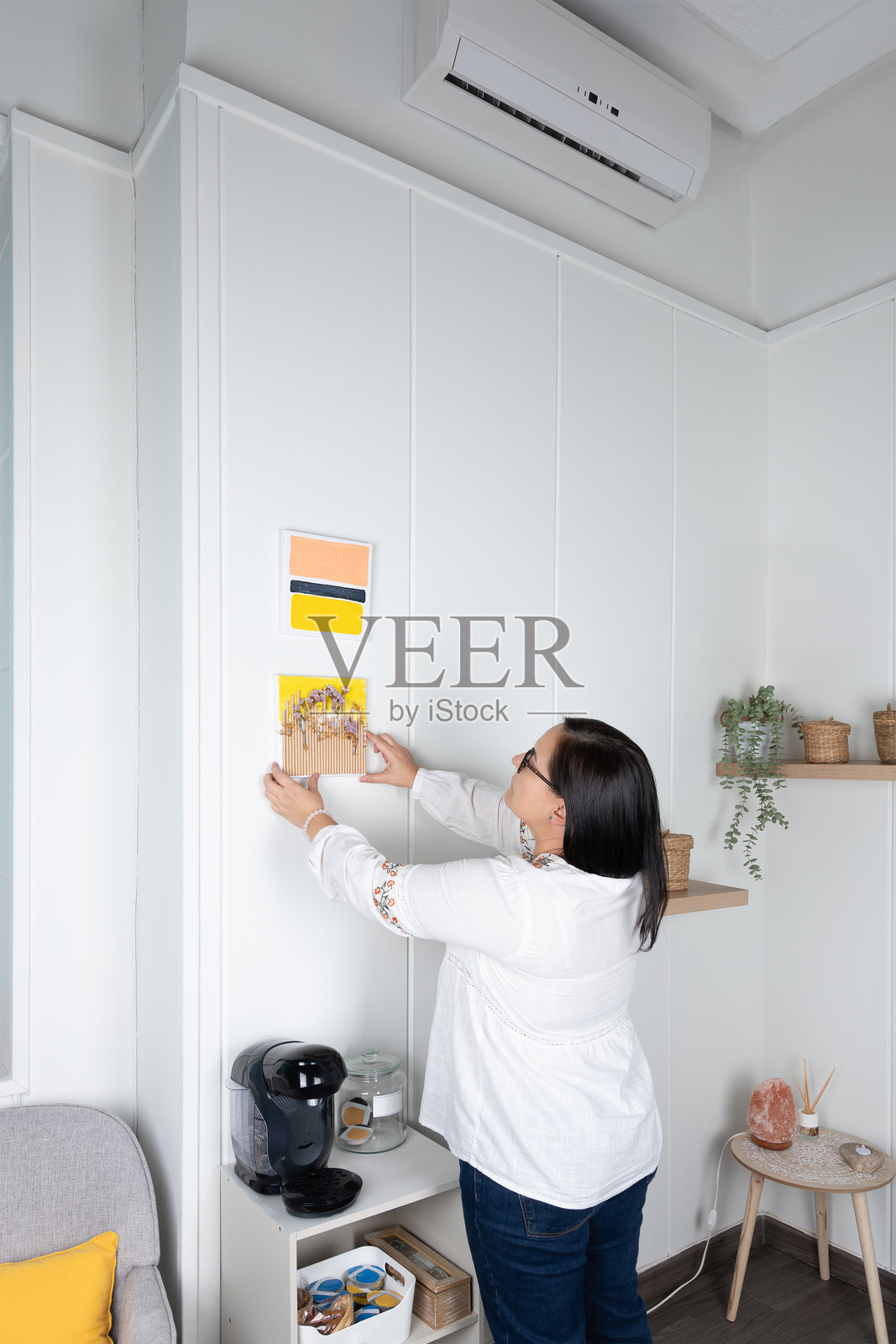 一位女性在极简风格的客厅墙上挂上自己制作的照片。照片摄影图片