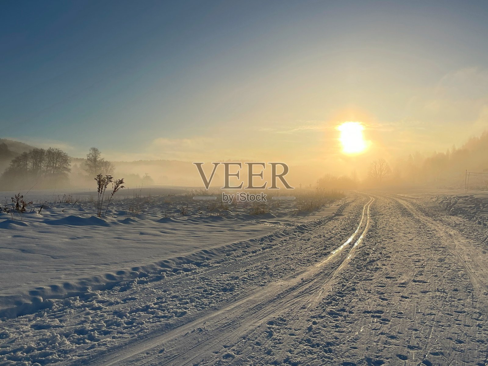 被雪覆盖的田野上有北欧滑雪轨迹,通向雾蒙蒙的地平线,映衬着挪威奥斯陆温暖的日出光辉。照片摄影图片