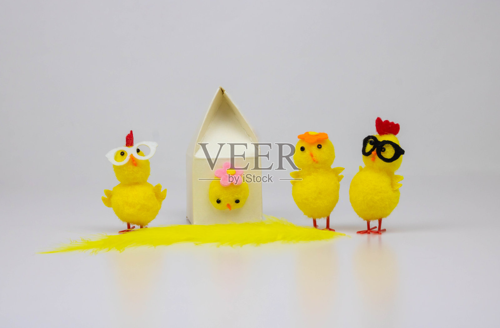 一个鸟屋和四只黄色玩具小鸡在白色背景下格外显眼。复活节的概念照片摄影图片