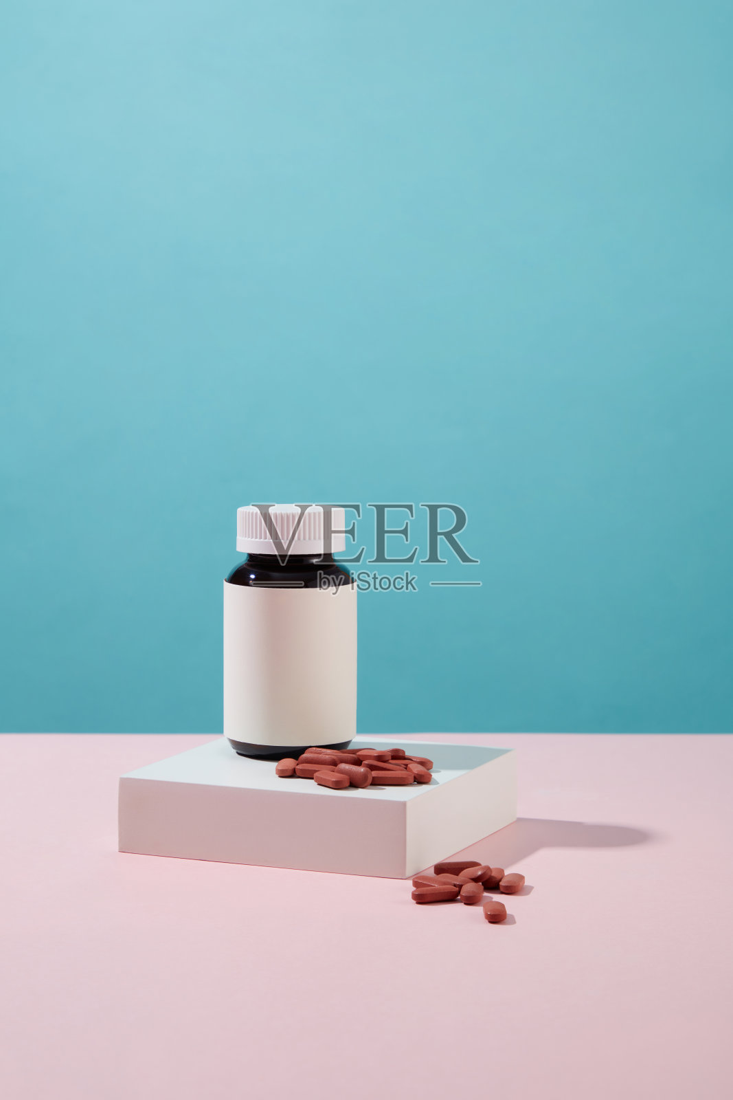 一个没有标签的药瓶的正面视图被放置在一个白色的讲台上,上面有红色的药片。蓝色和粉红色的背景。空白标签的新药广告模型。照片摄影图片