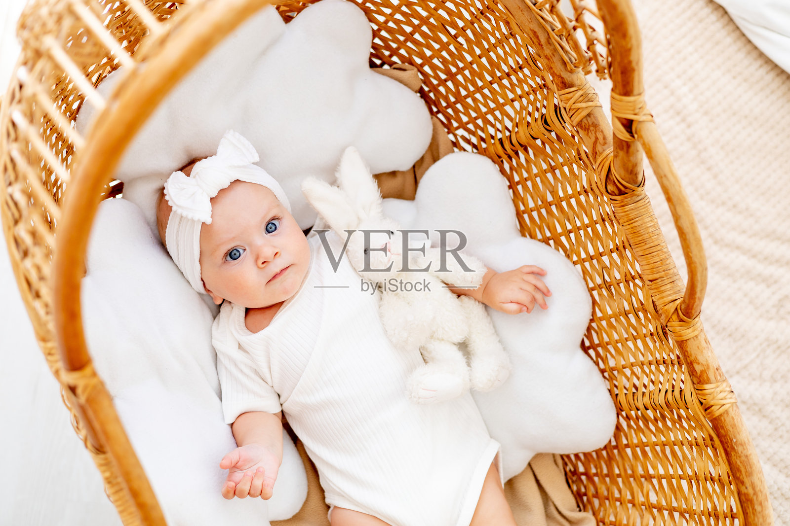 一个快乐的婴儿在柳条摇篮里微笑或大笑,抱着一只毛绒兔子,一个小女孩早上醒来或入睡,新生儿微笑,俯视图照片摄影图片