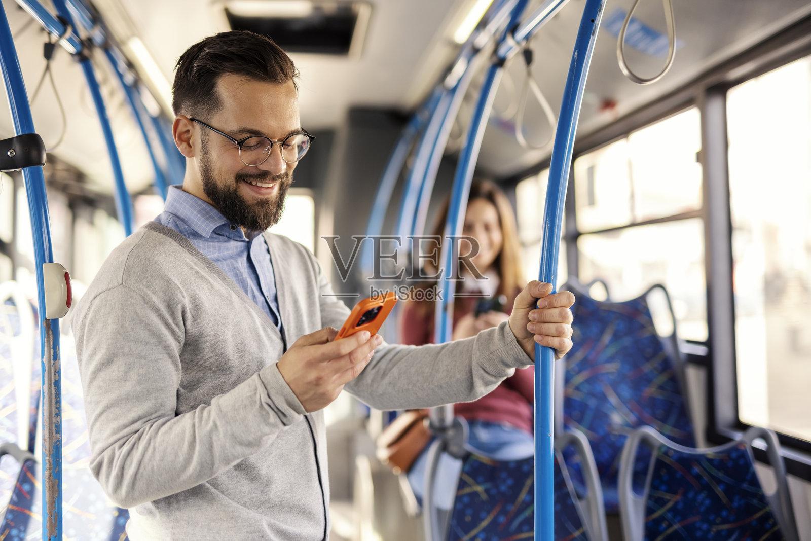 年轻通勤者在城市公交车上手持手机通勤的肖像。照片摄影图片