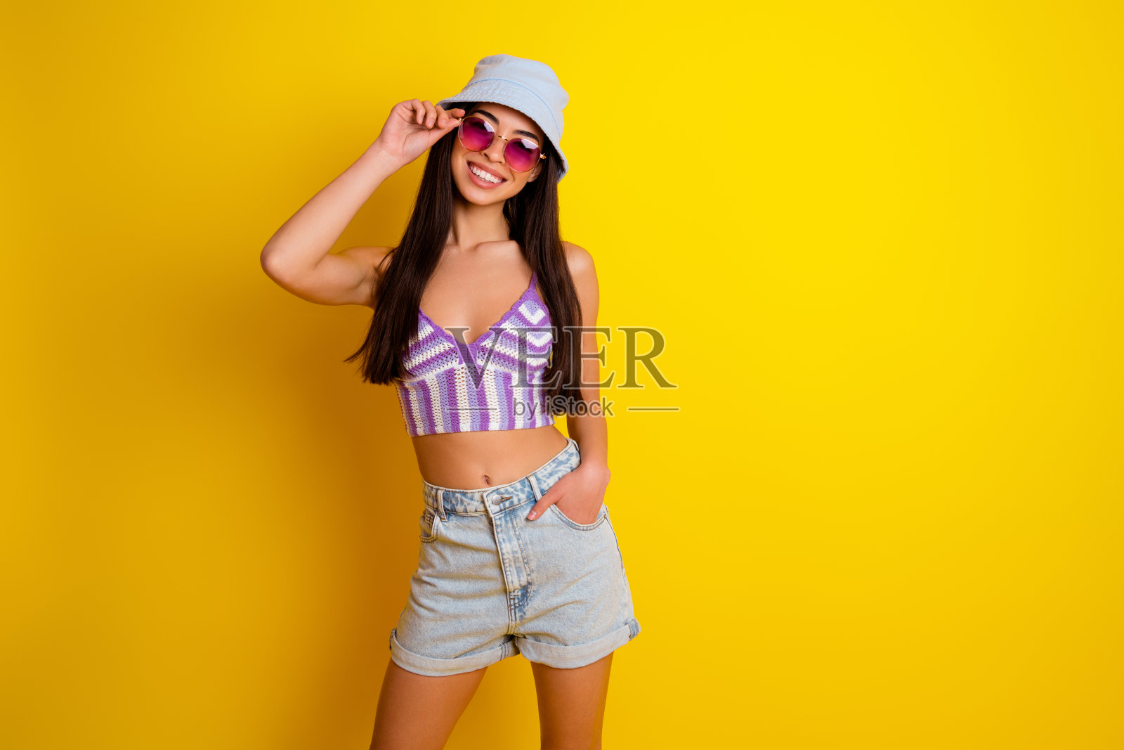 甜美迷人的女士穿着条纹短款上衣,戴着深色眼镜,背景为空旷的黄色。照片摄影图片