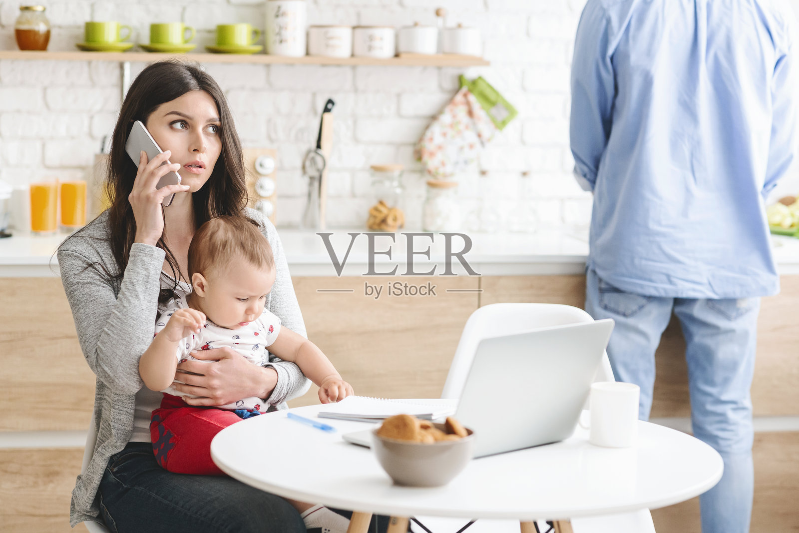 现代厨房环境中,女性一边抱着宝宝一边打电话。照片摄影图片