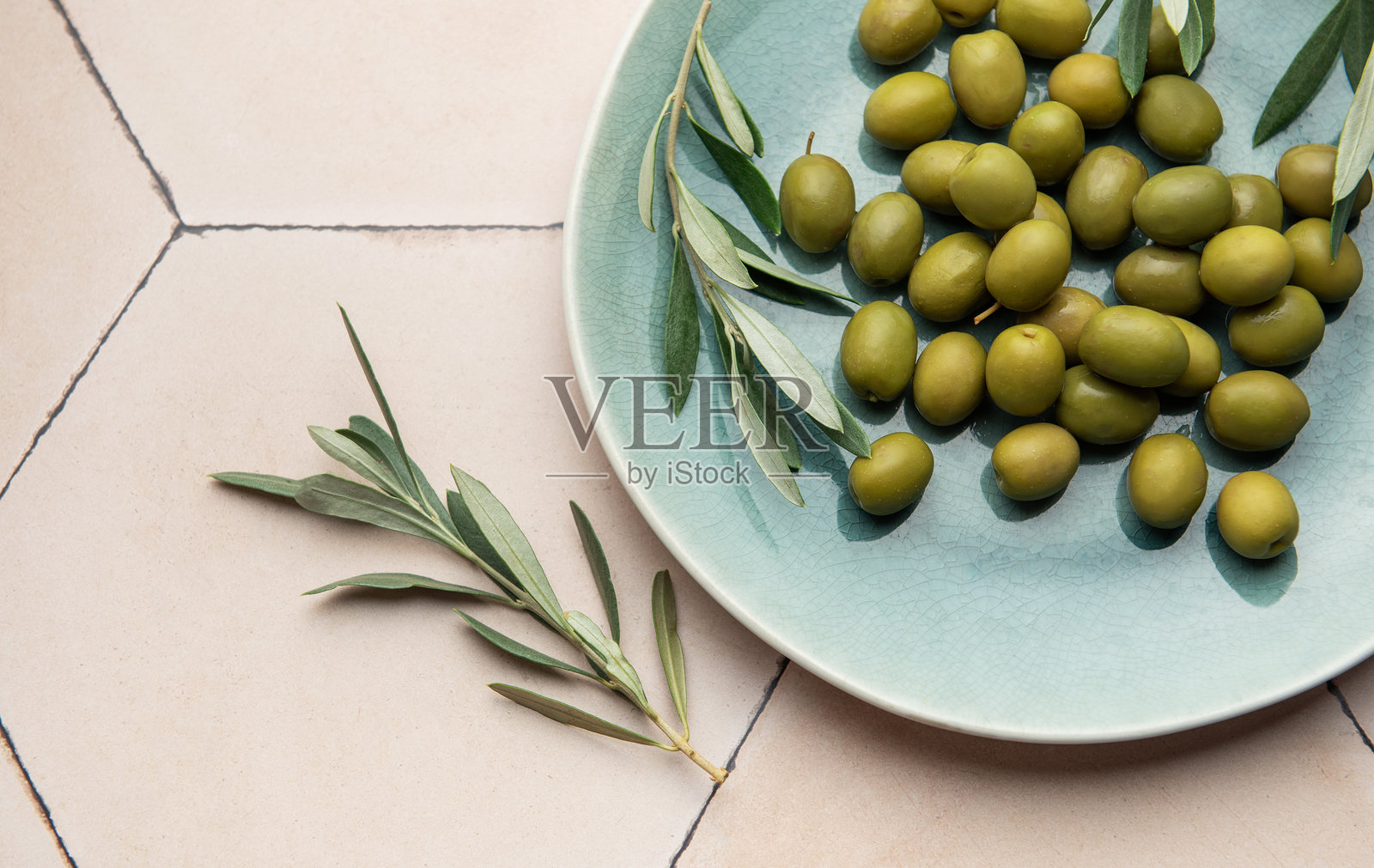 新鲜的绿橄榄与橄榄枝放在乡村风格的陶瓷盘上照片摄影图片