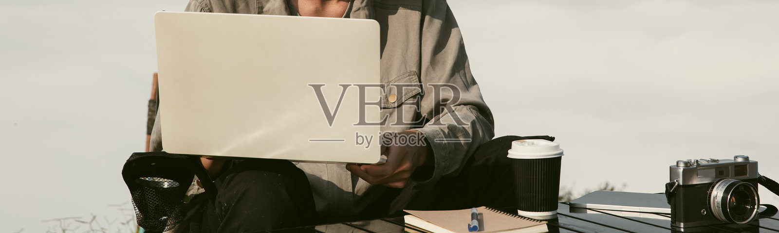 年轻商人在山顶使用电脑工作。徒步旅行者在日落时分使用笔记本电脑进行在线购物,山顶的日出,远程工作的自由职业者使用数字平板。旅行度假概念。照片摄影图片