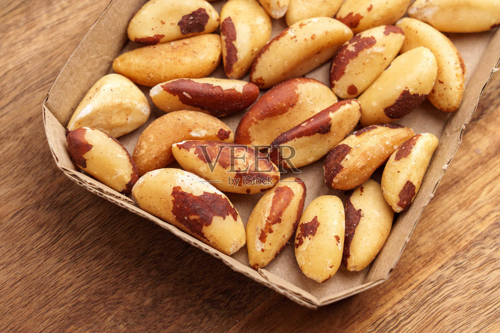 木桌上放着纸板托盘里的干巴西坚果。照片摄影图片