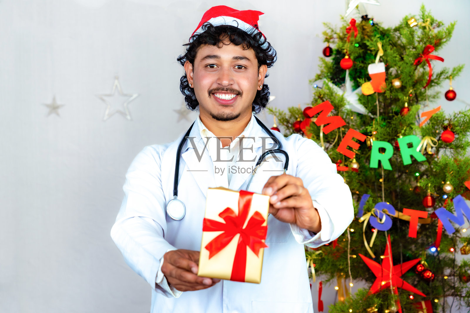 年轻男性医生戴着圣诞帽,手持礼物,节日与新年医疗医院概念照片摄影图片