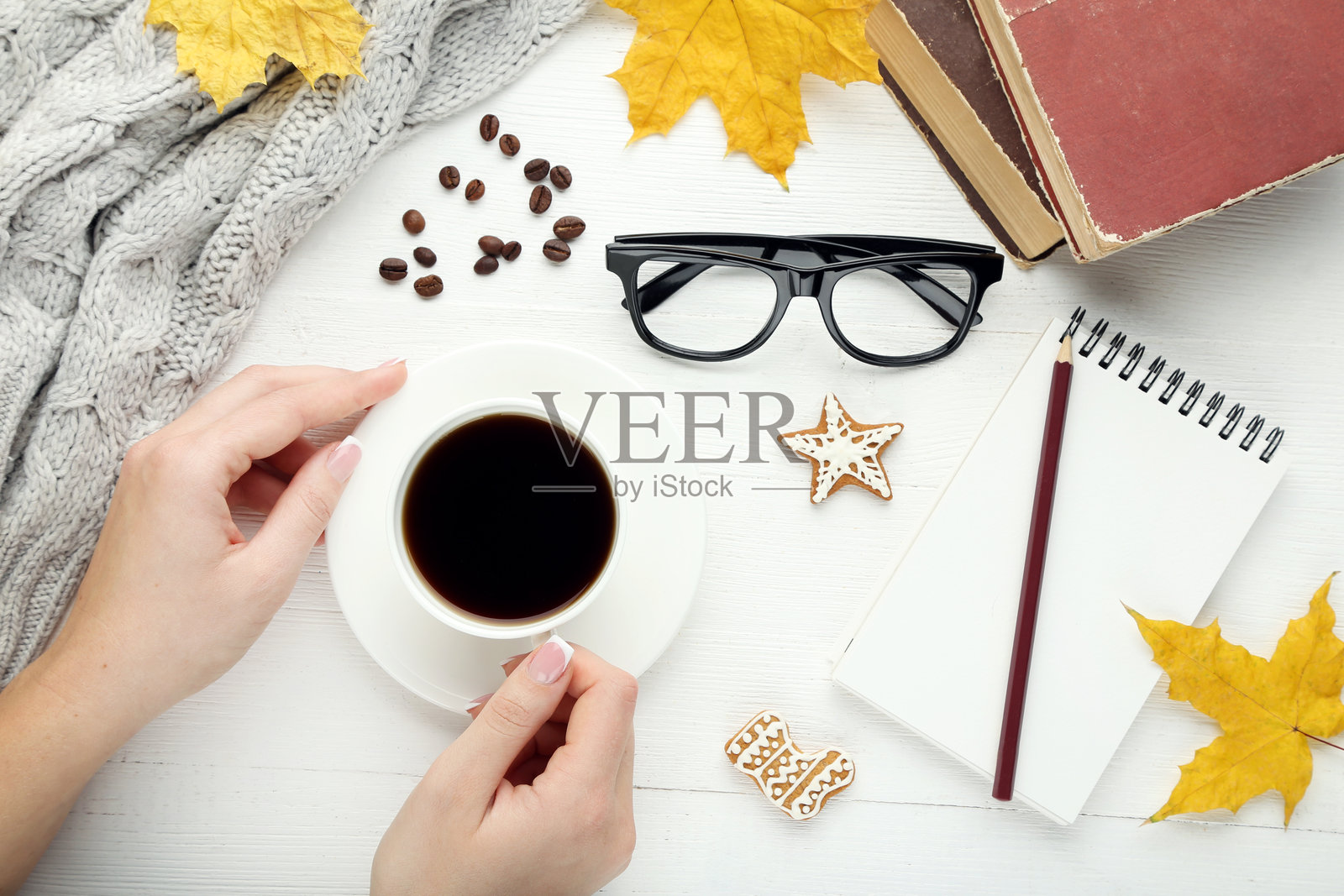 女性手握咖啡杯,旁边有姜饼饼干、笔记本和眼镜照片摄影图片