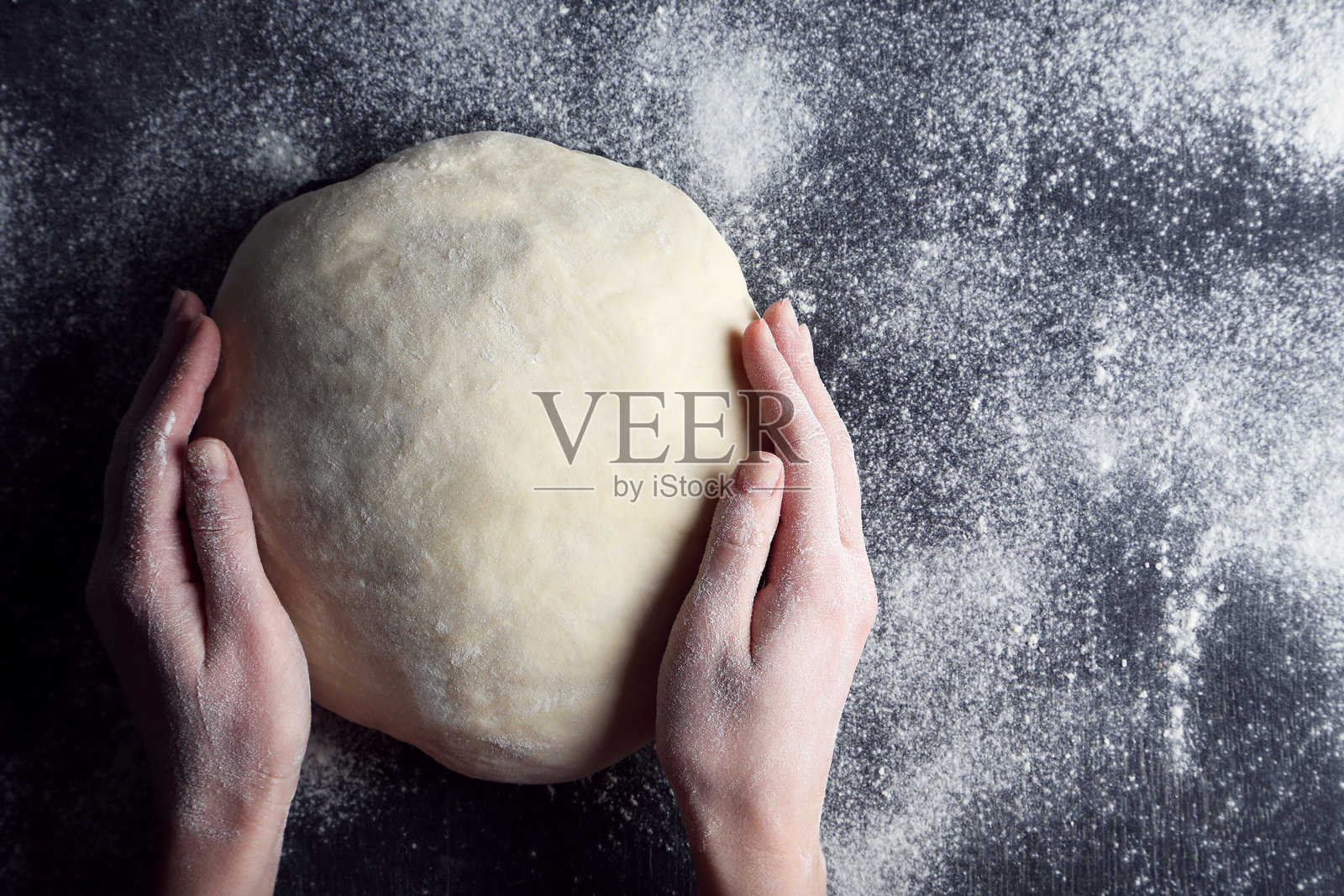 女性的手在黑色木桌上捏着生面团照片摄影图片