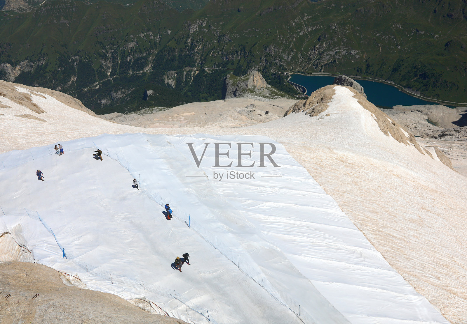 人们在阿尔卑斯山脉多洛米蒂山脉的马尔莫拉达山冰川上方安装的白色保护膜上行走,夏季时节。照片摄影图片