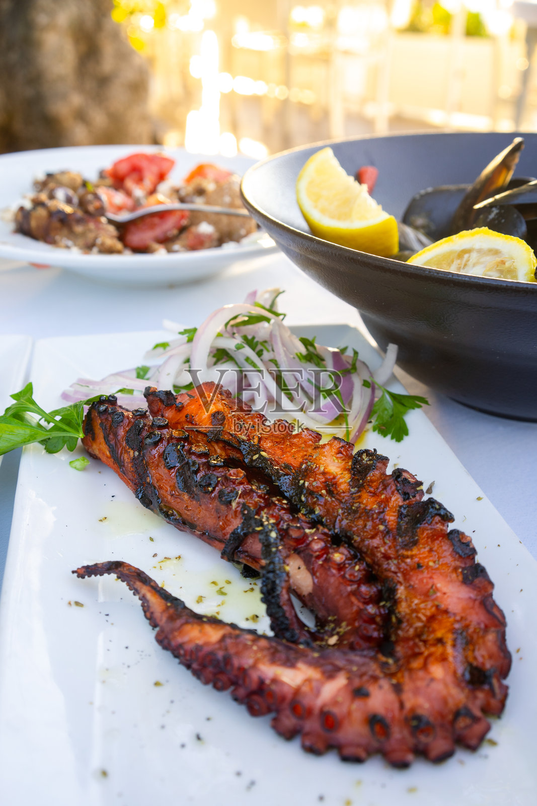 餐厅里提供的烤章鱼腿,配洋葱沙拉和旁边的贻贝。照片摄影图片