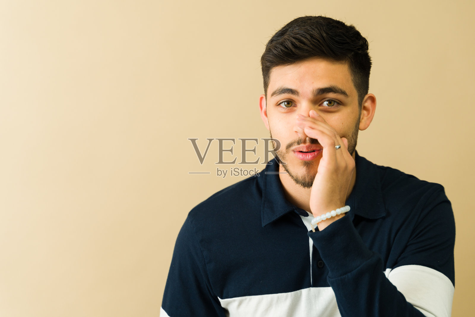 好看的年轻男子在米色背景上低声说秘密照片摄影图片