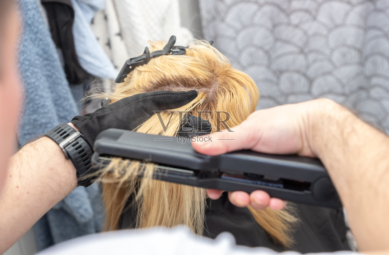 男性发型师正在用直发器为女性拉直头发。照片摄影图片