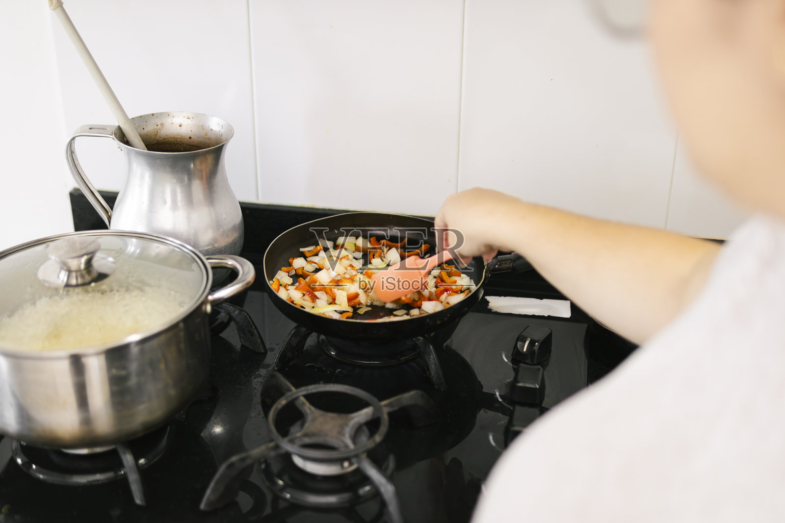 拉丁裔女性在炉灶上用平底锅炒洋葱和辣椒照片摄影图片