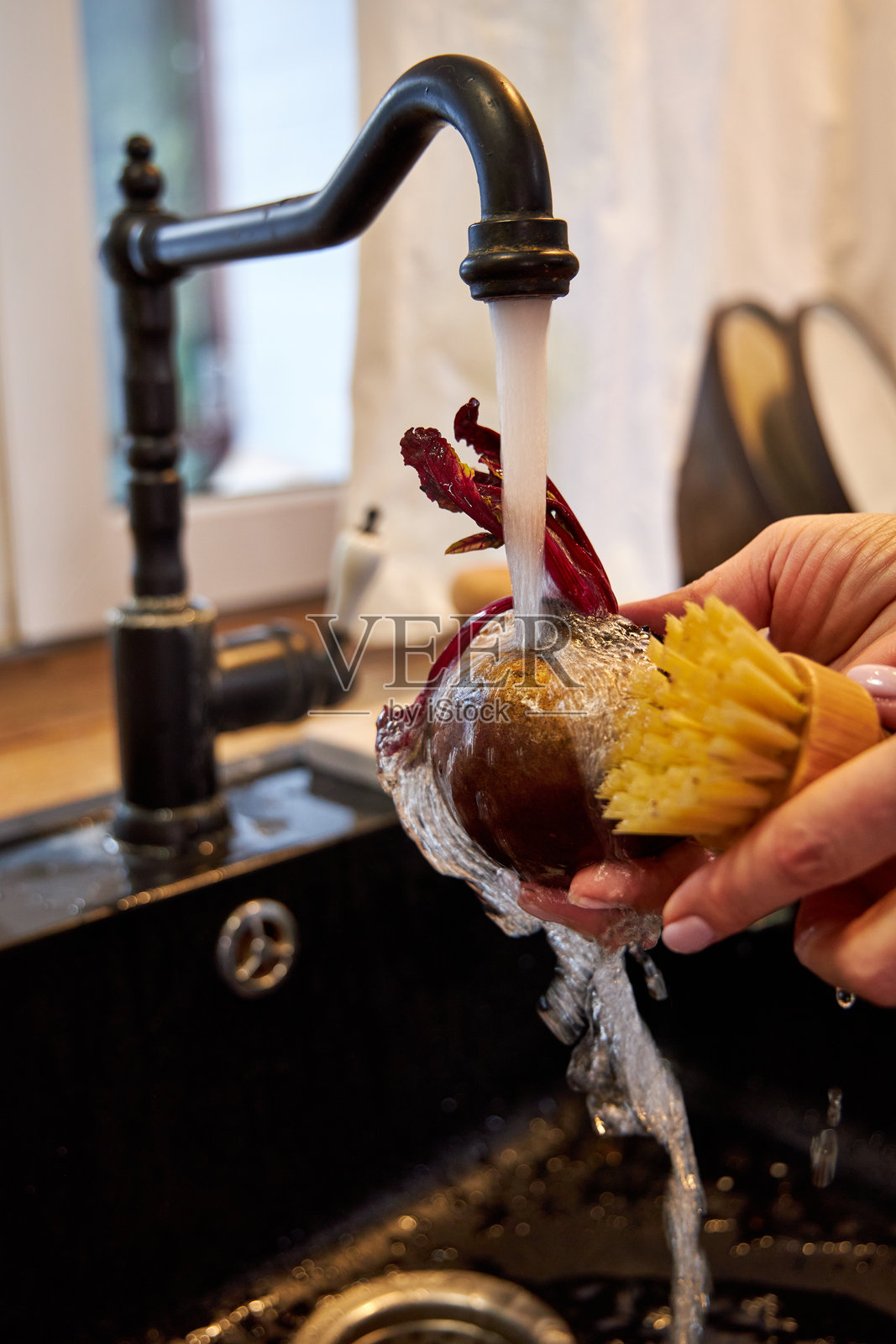 一位女性在现代黑色水槽中用木刷清洗蔬菜和甜菜。照片摄影图片