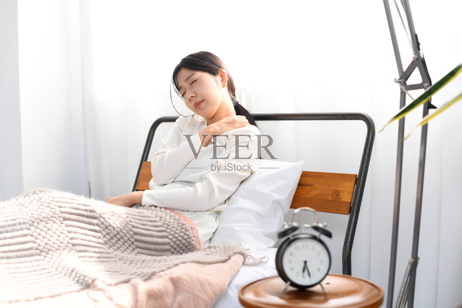 疲惫的亚洲年轻女性在床上因肩部僵硬而痛苦照片摄影图片