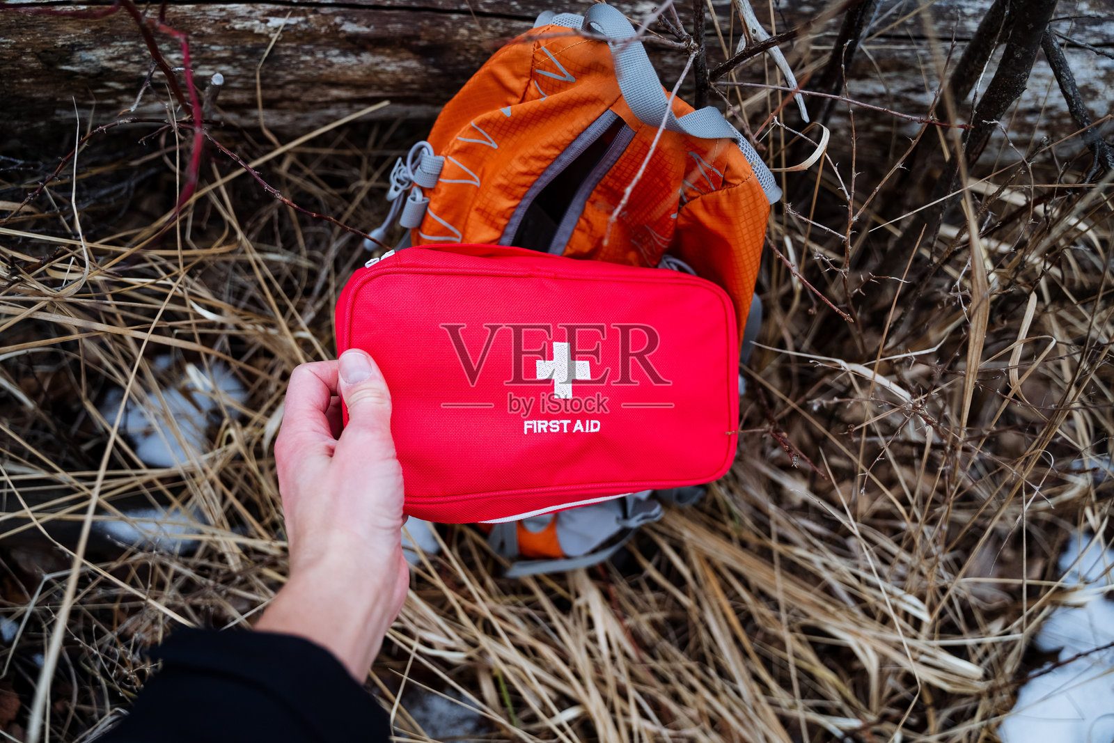 一个人站着,手里拿着一个鲜红色的急救包,正好在一个橙色背包前面,这为整体场景增添了色彩和背景,同时展示了必要的物品。照片摄影图片
