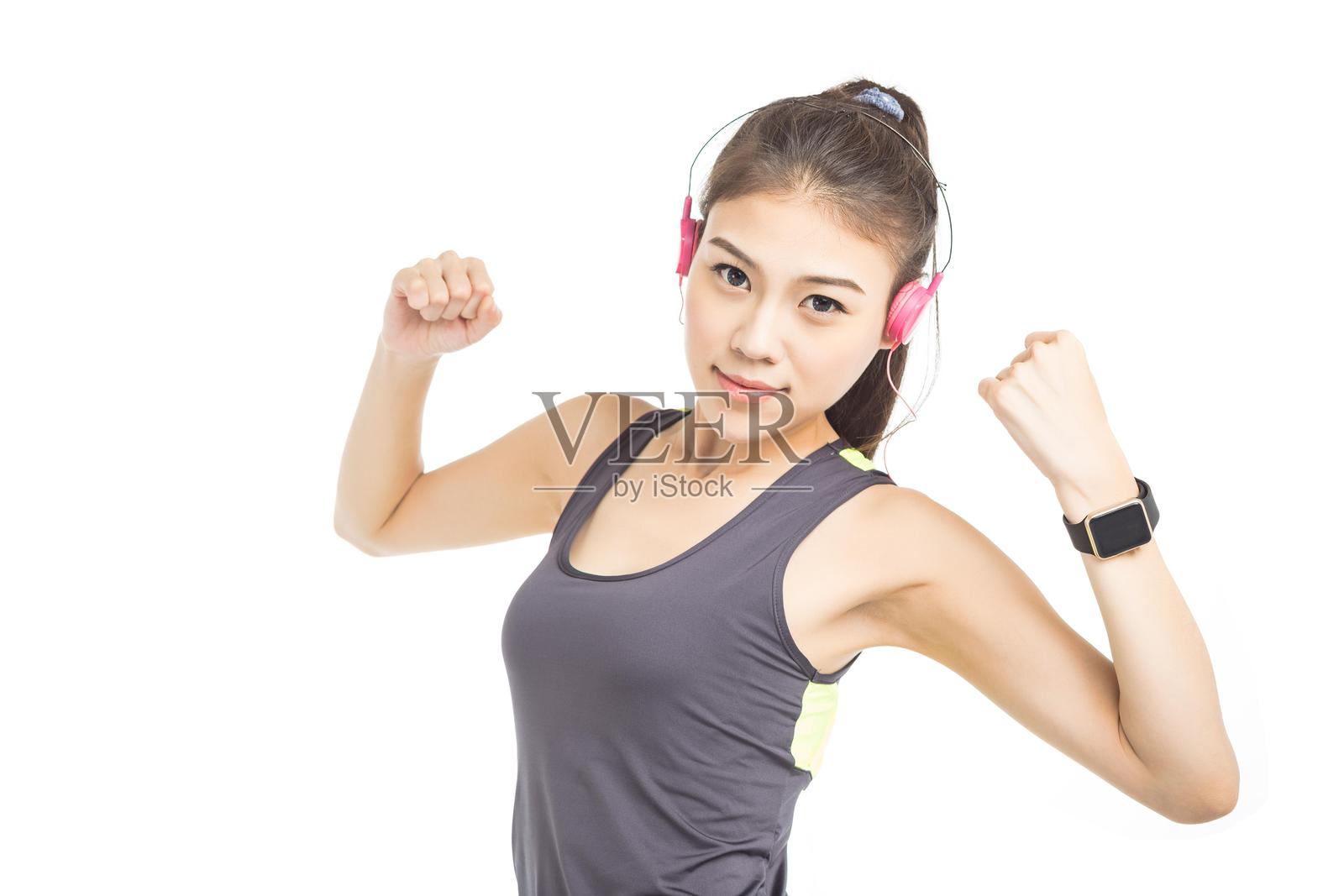 穿着运动服的亚洲女性戴着耳机和智能手表,展示她的肌肉。照片摄影图片