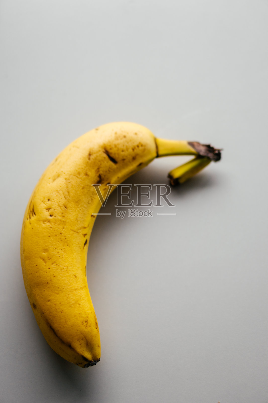 一根表皮有黑点的非常成熟的黄色香蕉特写,背景为灰白色,是一种有争议的食物。照片摄影图片