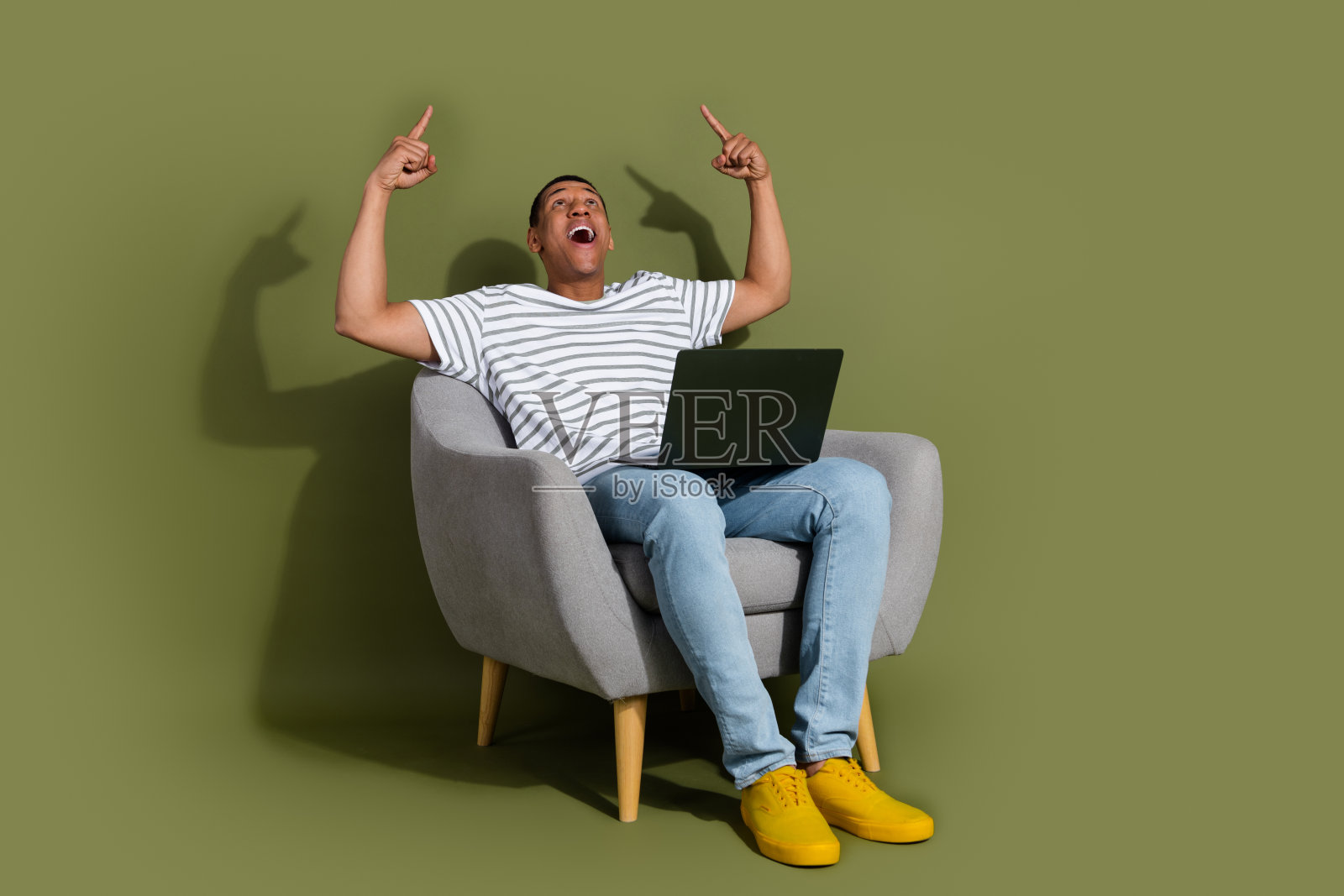 全身照,吸引人的幽默男士穿着条纹T恤,手持现代设备,指向空旷的空间,背景为卡其色。照片摄影图片