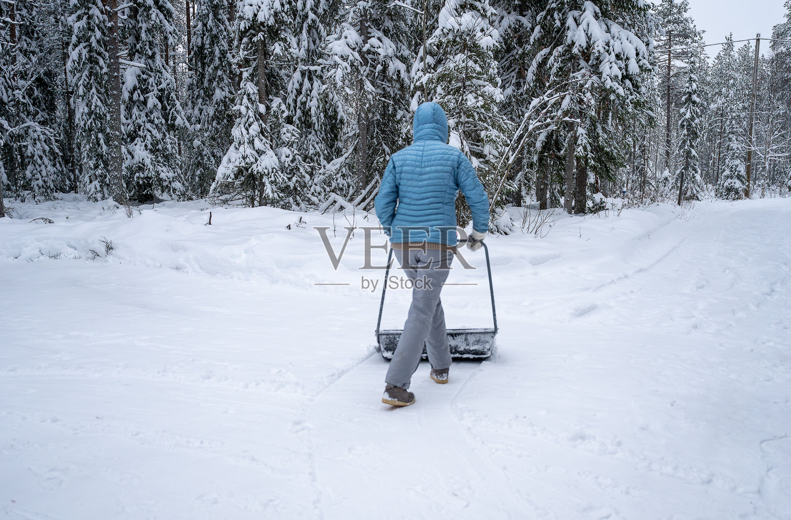 穿着冬季服装的女性在户外用刮雪器清理积雪照片摄影图片