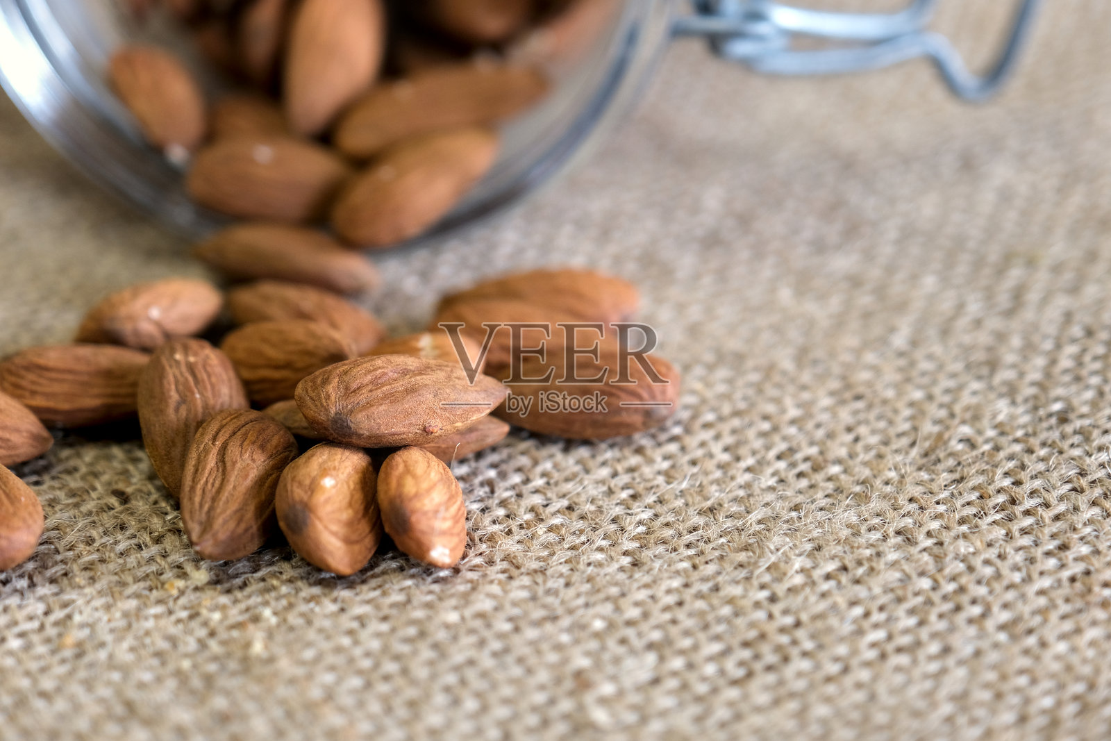 一个玻璃罐翻倒,生杏仁洒落在有纹理的麻布表面上照片摄影图片