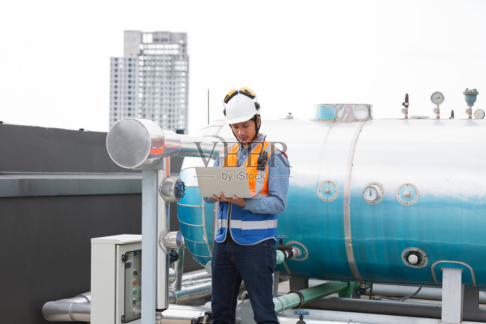 男性工程师在施工现场的下水道区域使用笔记本电脑进行检查或维护。男性水管工在建筑物的屋顶下水道区域工作。照片摄影图片