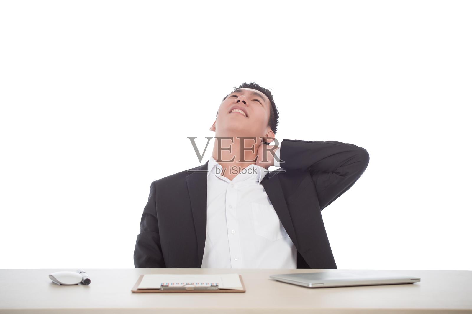 年轻的商人坐在桌子旁,手放在脖子上,抬头看着。照片摄影图片