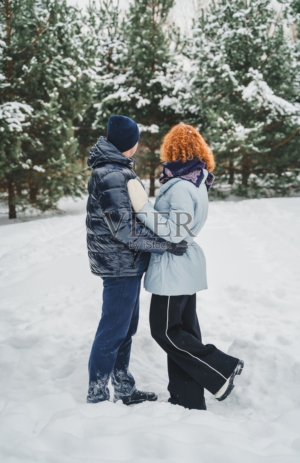 浪漫爱情故事。快乐的中年千禧夫妇,冬季雪地公园里一位红发女子。浪漫约会,亲吻,拥抱。散步,享受乐趣。时尚的蓝色衣服,夹克,帽子。照片摄影图片