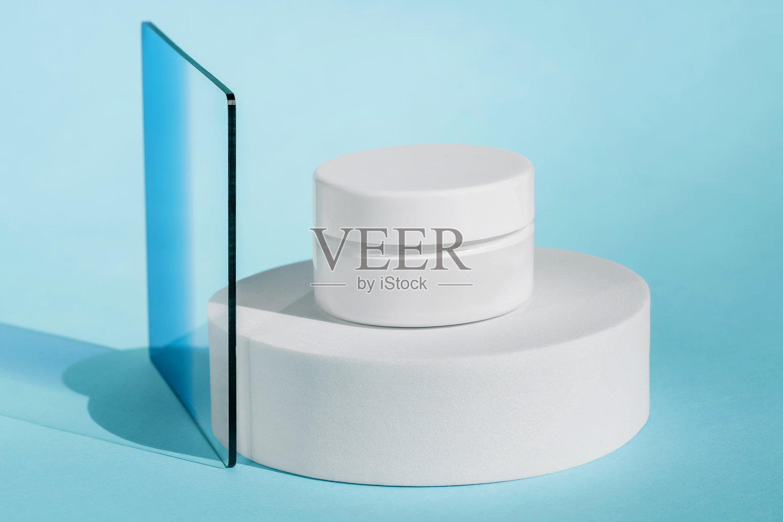 放置在圆形白色展示台上的紧致霜,搭配蓝色玻璃面板,干净现代的美学。照片摄影图片
